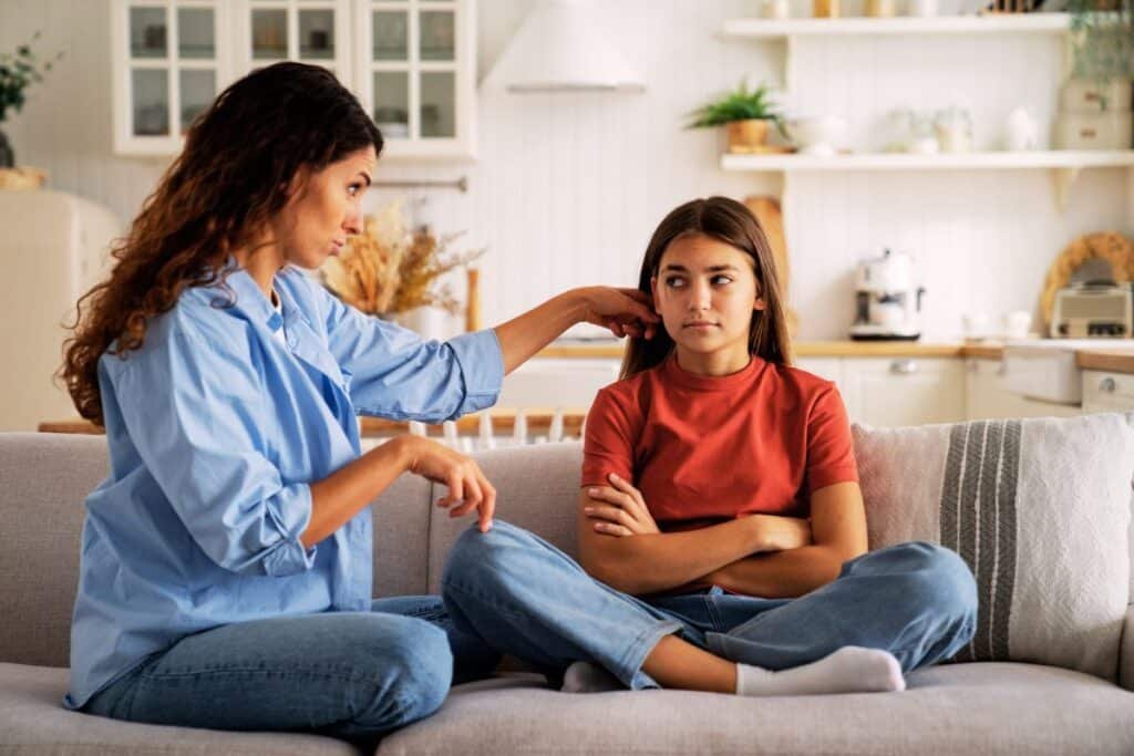 Mother with brown hair in a blue shirt speaking to a daughter with long brown hair and in a red shirt because she is concerned her child is being groomed