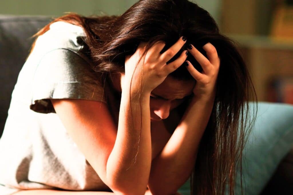 Teenager in grey tshirt and brown hair sat with head in hands