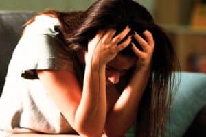 Teenager in grey tshirt and brown hair sat with head in hands