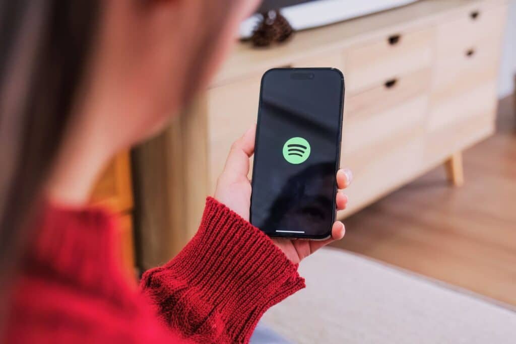 Woman in red jumper browsing Spotify on her phone