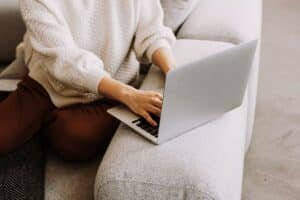 Woman in white jumper and brown trousers typing on MacBook