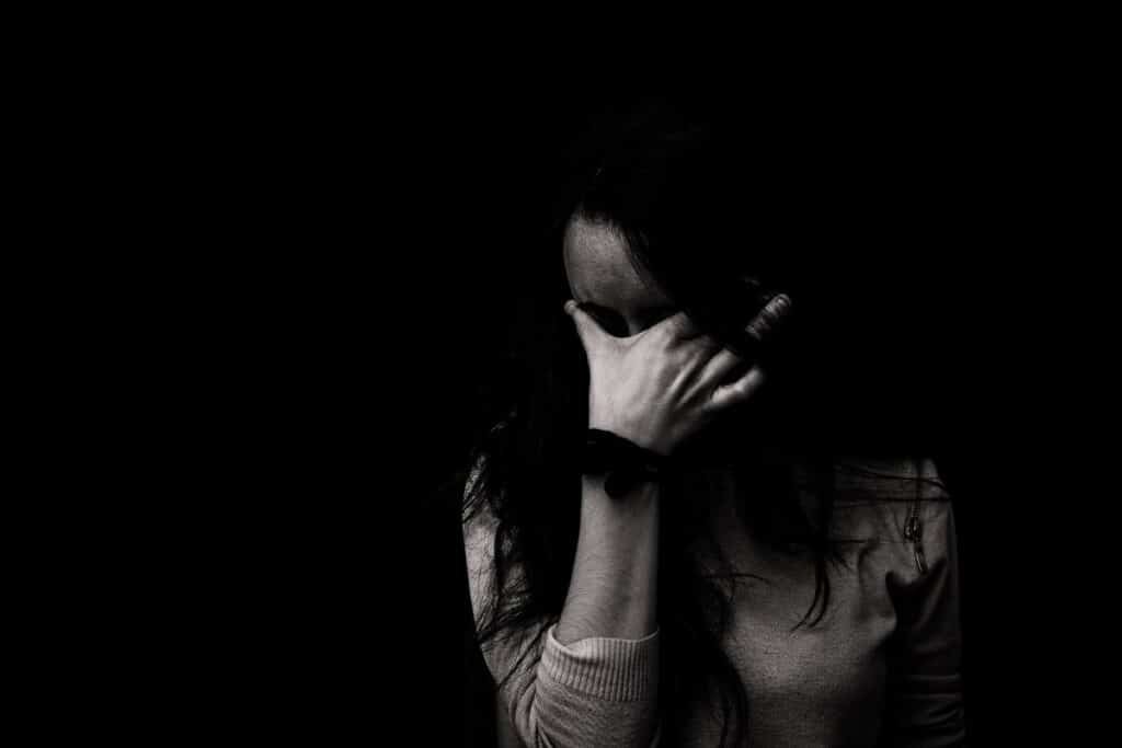 female in the shadows with her face covered with her hand