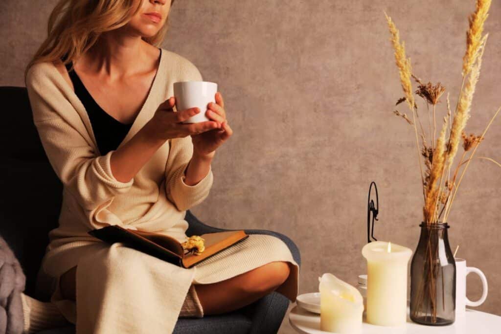 woman sitting with a cup of tea, candles, and a journal